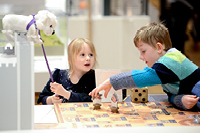 A little girl plays with a Boye the dog toy while a boy plays a Pikes and Ladders game